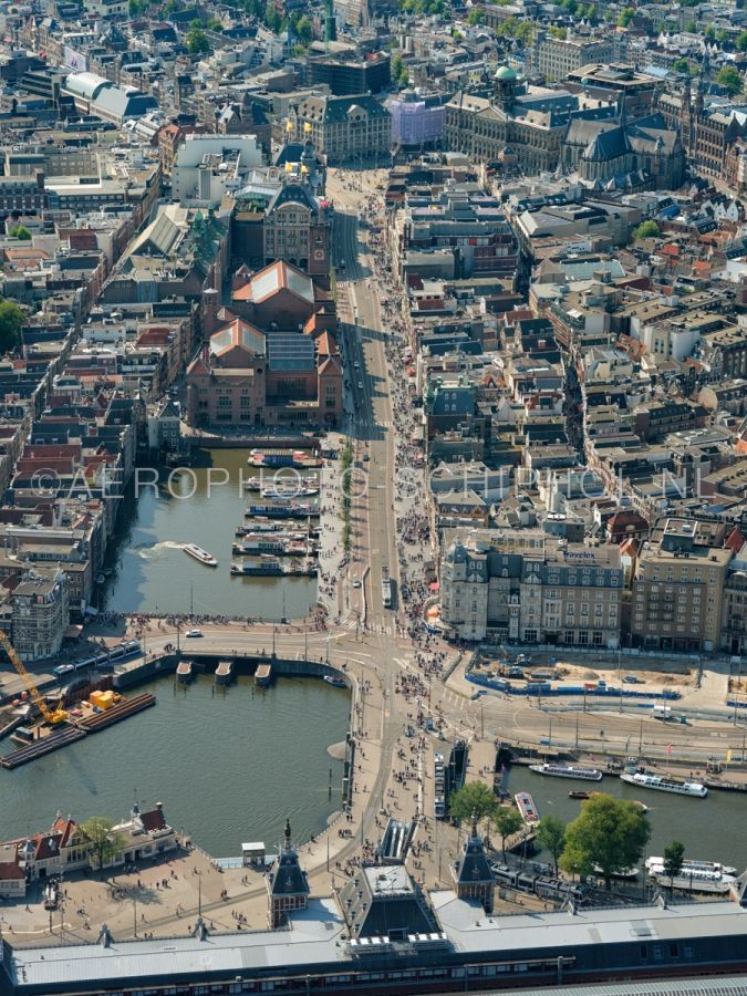 luchtfoto |  Amsterdam, Damrak gezien vanaf Amsterdam Centraal Station met boven in beeld de Dam. Het Damrak was voor het gedempt werd  tussen 1845 en 1883 het stuk van de rivier de Amstel tussen de sluizen op de Dam en het IJ opn. 02/09/2018